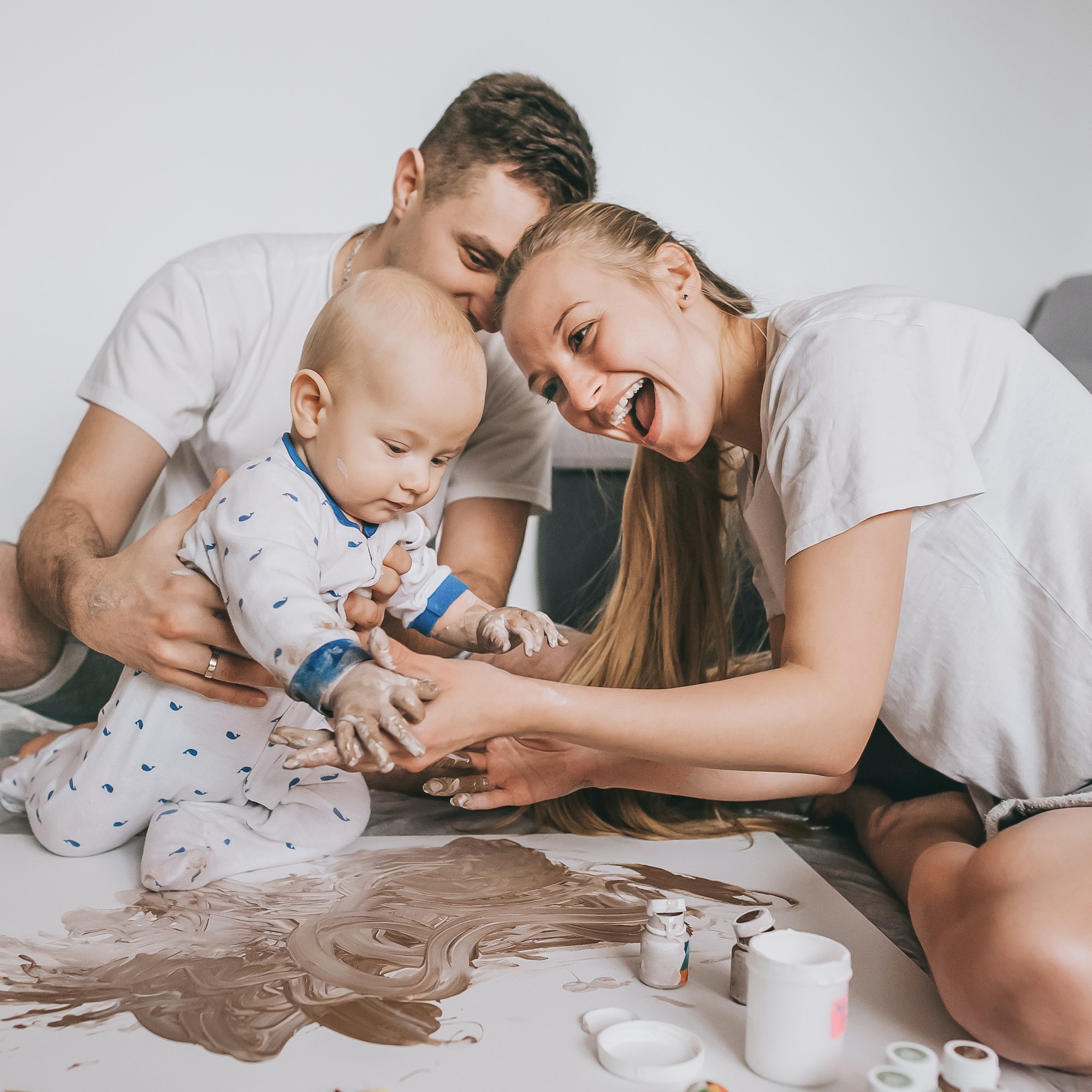 happy young family with adorable infant child painting together on floor at home