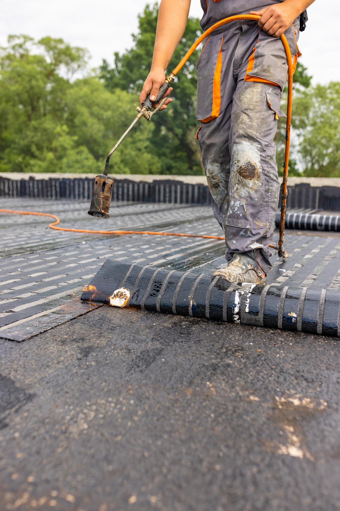 Workers placing a vapor barrier on the roof using a propane gas torch for welding bitumen sheets